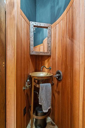 Decorative vessel sink with wall mounted faucet and stand, hickory paneled wainscotting, and travertine mosaic tile flooring