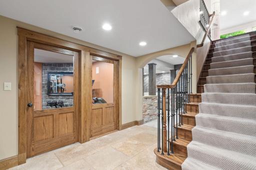 Staircase has oak railings with iron balusters and leads to the Exercise Room with partial glass door and wall.