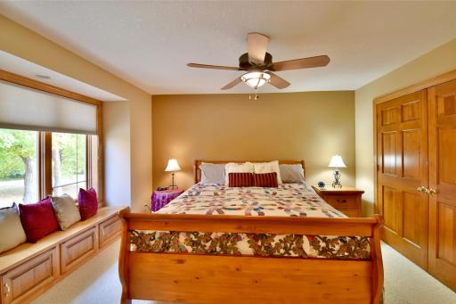 Upstairs bedroom with custom blinds, built-in sitting area, neutral decor, spacious closet, overlooking front yard.