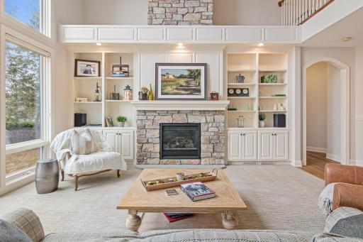 Beautiful living room featuring a wall of windows with panoramic lake views, custom built-ins, and a gas-burning fireplace for cozy yet elegant living.