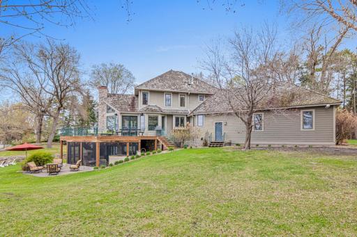 Beautiful park-like yard with views of the home’s stunning exterior, patio, deck, and screened porch—complete with a meandering trail leading down to the lake for the ultimate in outdoor living.