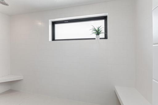 Thoughtfully curated walk-in shower includes a window for natural light, a convenient shower bench, and a stable foot stop for shavingâcombining practicality with elegance