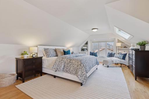Third floor primary suite with vaulted ceiling, hardwood floors, skylight, built-in window seat and shelving, a walk-in closet, and 3/4 bath.