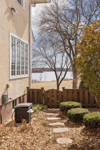 The side yard is professionally landscaped with stone pavers leading to a front patio overlooking the lake and additional gardens.