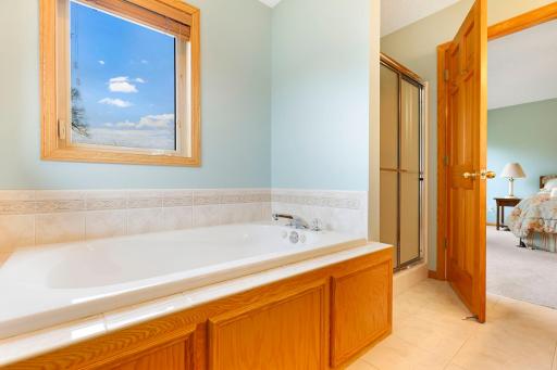 Jetted tub situated on a tile deck and surround and separate shower w/ privacy glass doors