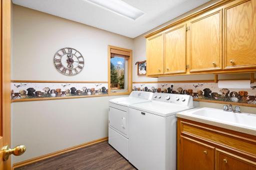 Laundry room with oak cabinetry offers storage and a drop-in utility sink. Luxury vinyl flooring