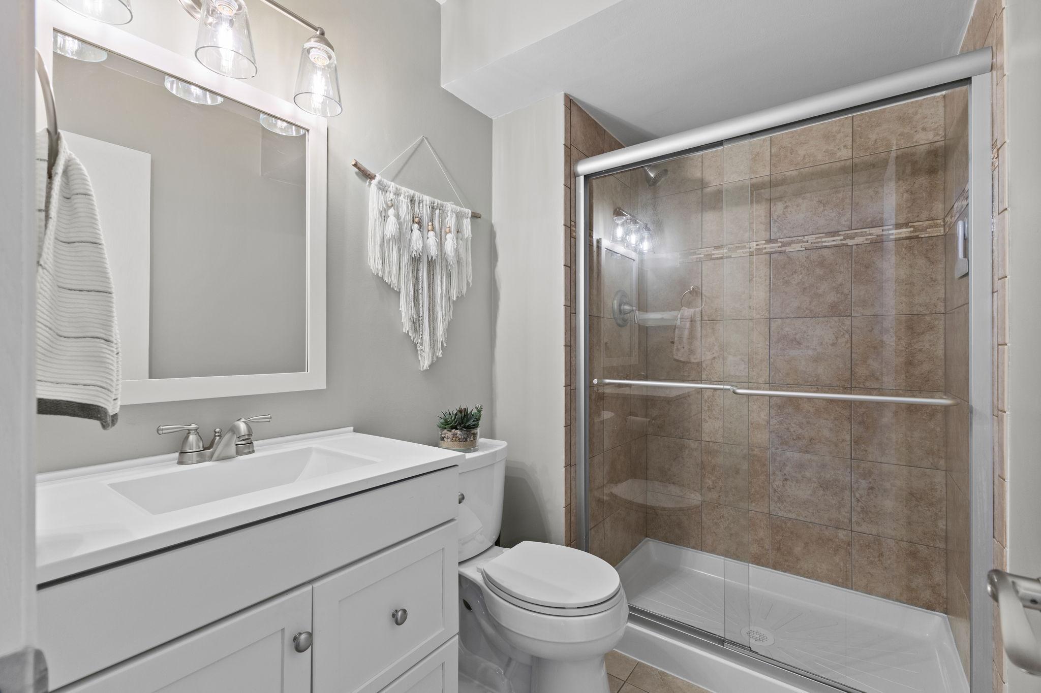 This is the lower level 3/4 bathroom with a stylish and functional space featuring a modern white vanity with ample storage, complemented by a tile surround shower with a glass door.
