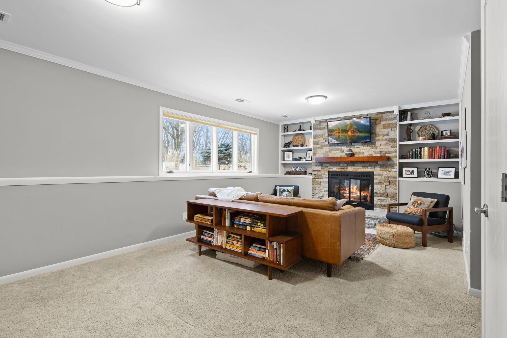 The lower level family room! The stone fireplace is a stunning focal point. Built-in shelving adds functionality and charm, offering space for personal touches. Large windows flood the room with natural light, making it feel bright and airy!