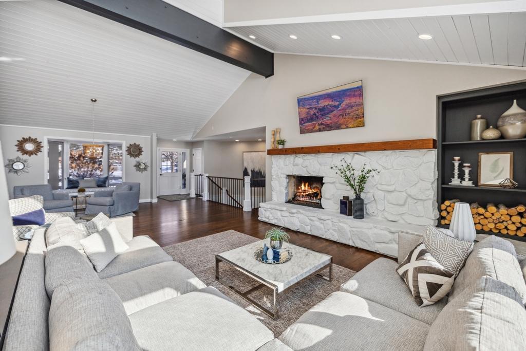A striking gas fireplace framed by a stacked stone surround and reclaimed wood mantle anchor the space, while soaring vaulted ceiling with shiplap detailing and a beautifully crafted wood beam add warmth and architectural interest.