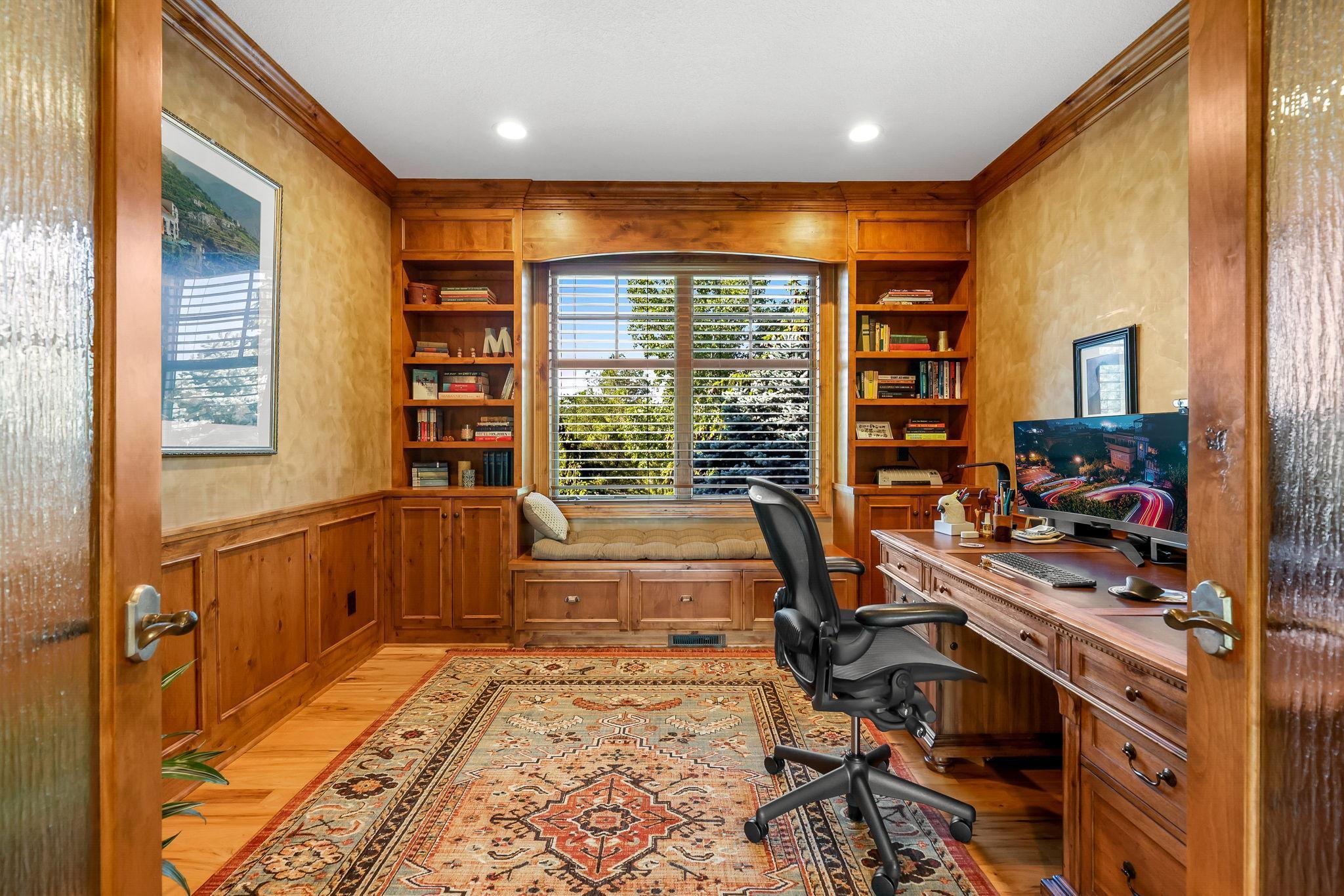 Spacious main floor office – located next to the primary bedroom and offers Alder wood built-ins and bench, and serene views of the extensive front landscaping.