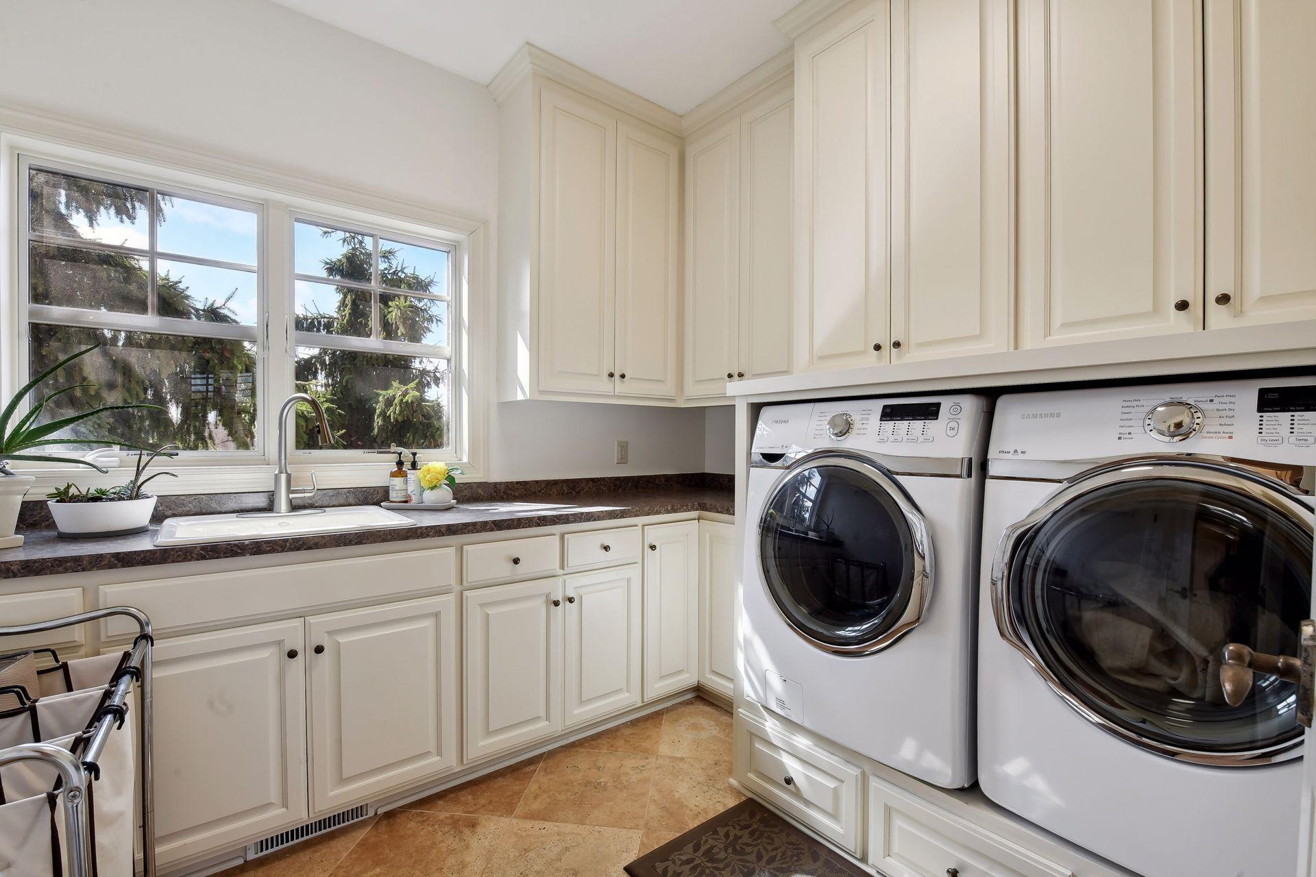 Main floor Laundry room with an abundance of countertop and cabinet space, a sink, and large Samsung washer/dryer units.