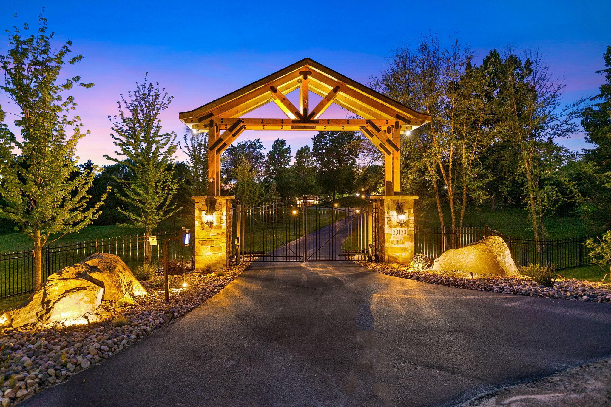 Evening brings a whole other level of beauty to this property! Majestic front entryway with electric gate mirrors the construction of the outdoor kitchen, built with a solid concrete foundation and steel below the frost line.