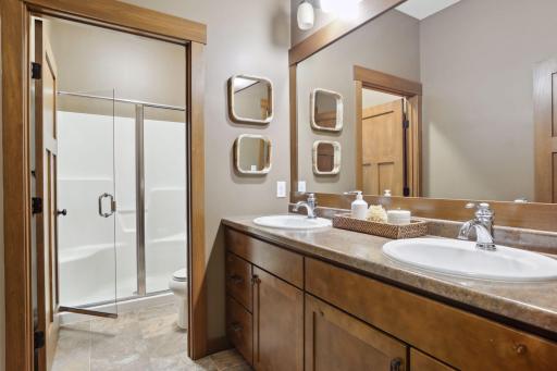 The lower level bathroom offers a dual bowl vanity with ample storage and a private, compartmentalized shower and toilet area, blending function and convenience.