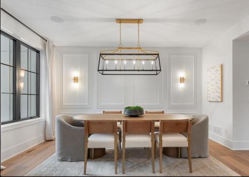 Dining room features paneled walls , hardwood flooring, and wall sconces.