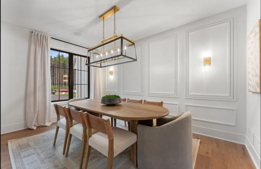 Dining room features paneled walls , hardwood flooring, and wall sconces.