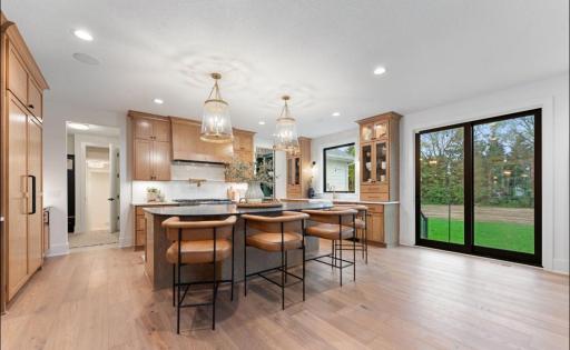 Custom designer kitchen features white oak cabinetry, large island with arched quartz seating area, full size frig and freezer columns with wood panels, ice machine, glass rinser, apron sink and painted prep pantry.