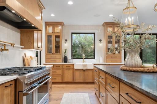 Custom designer kitchen features white oak cabinetry, large island with arched quartz seating area, full size frig and freezer columns with wood panels, ice machine, glass rinser, apron sink and painted prep pantry.