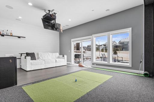 Golf simulator room offers elevated spectator seating, bar stools plus a walkout to the back patio