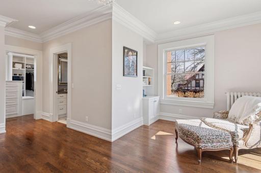 Primary bedroom suite featuring a sitting area, built-in shelving, a large walk-in closet with center island storage and built-in bench and a luxurious en suite bath.