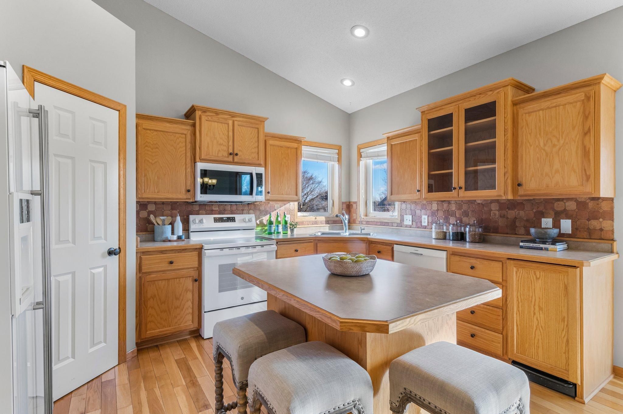 The kitchen features vaulted ceilings, rich wood flooring, and abundant oak cabinetry with under-cabinet lighting. It also features a spacious 4x4 pantry, a reverse osmosis water system, and a large center island with breakfast bar seating.