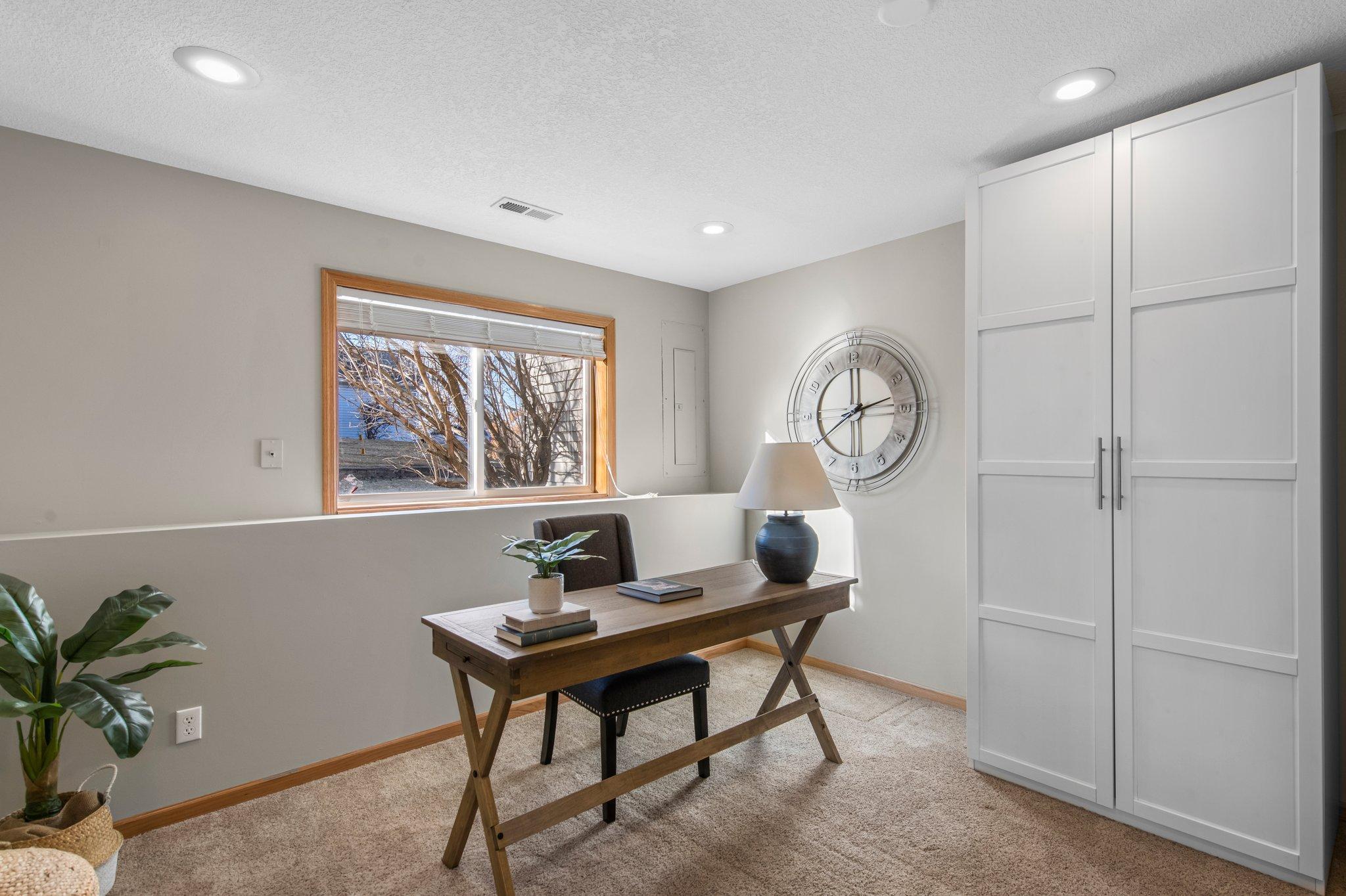 The lower-level bedroom, which could also serve as an office, is carpeted and features a large wardrobe cabinet, glass French doors, and a private half-bathroom.