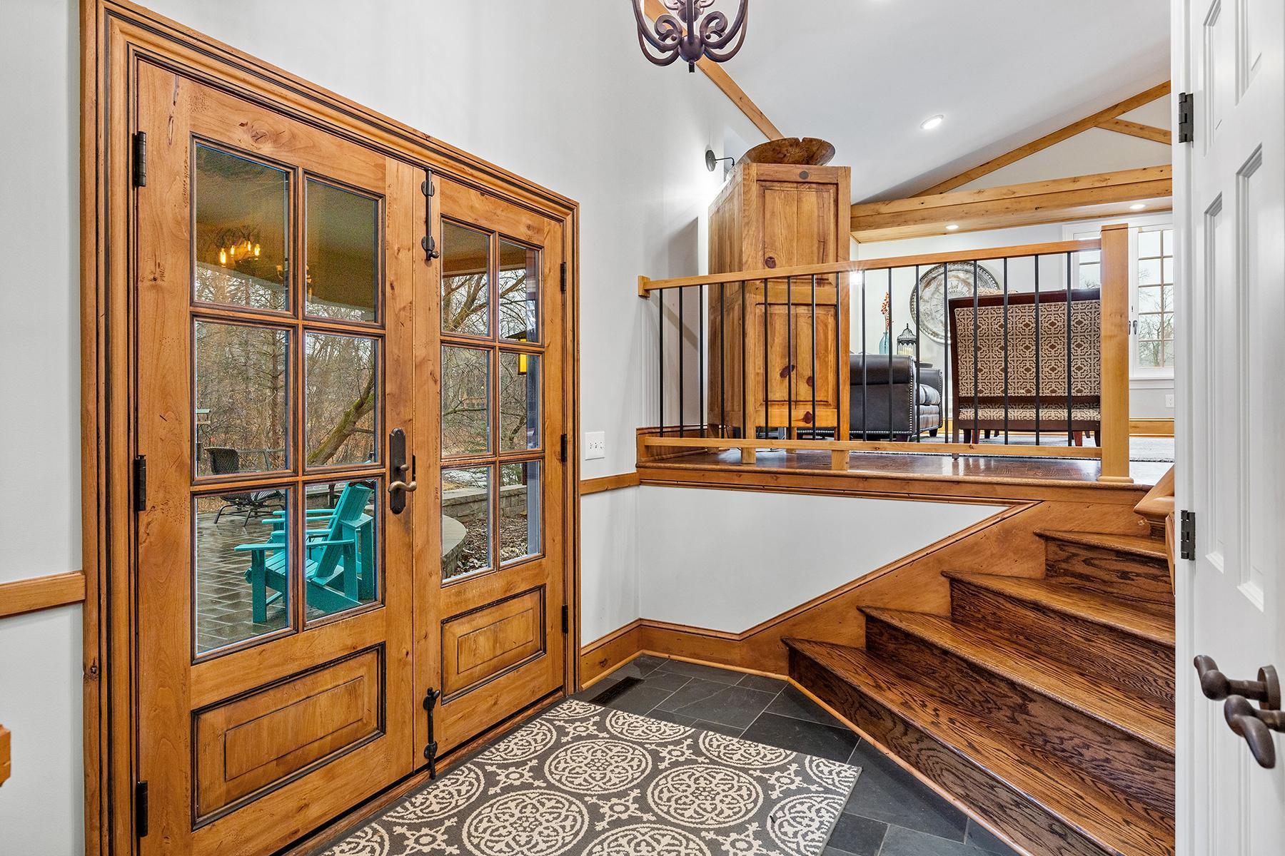 Large welcoming foyer with slate tile, rich wood and glass paneled double doors.