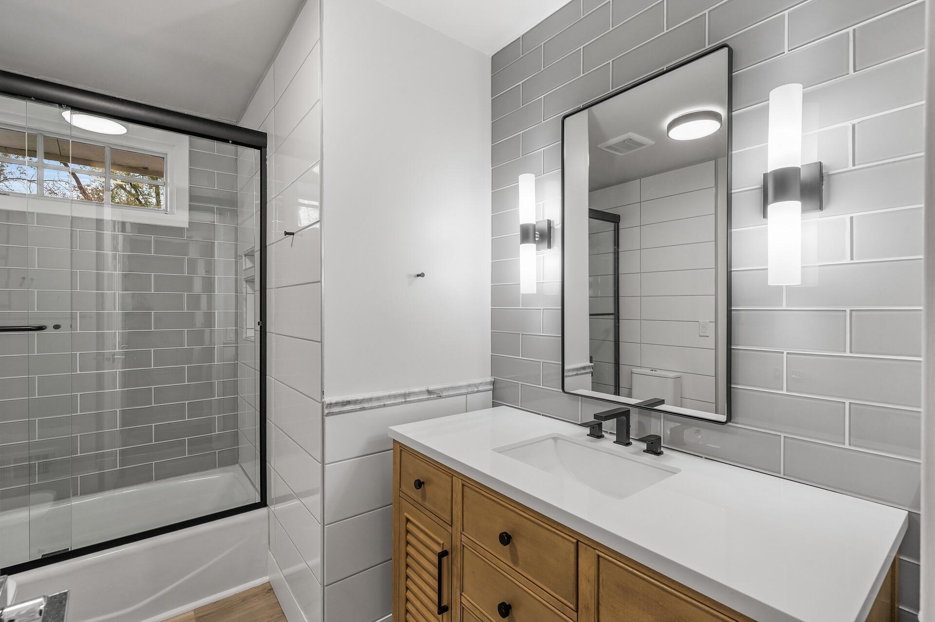 This nicely updated full bath features a stylish tiled shower surround, elegant tiled accent walls, and an updated vanity and flooring.