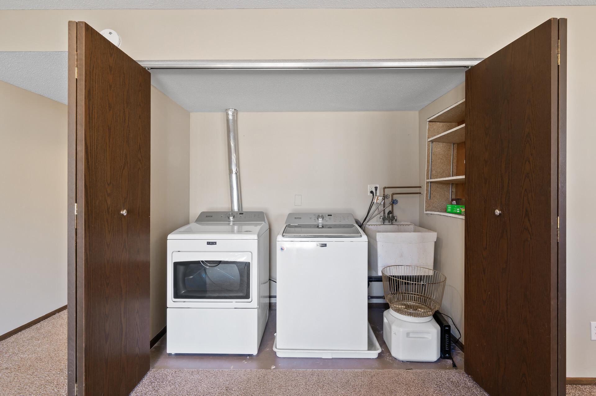 Here you will see the laundry closet includes a convenient utility sink, built-in shelving for laundry supplies, and a newer washer and dryer.