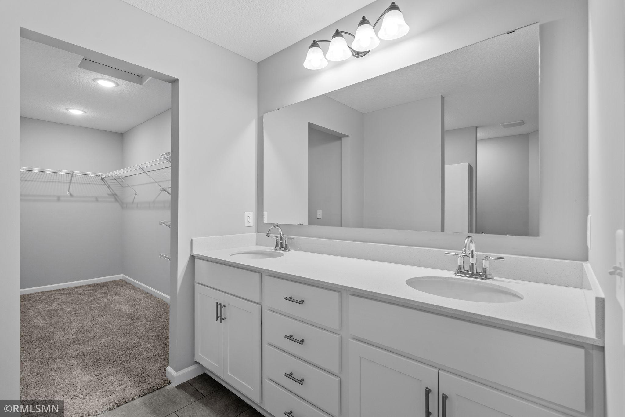 (Photo of previously finished home) The luxurious owner's suite features a spacious, elegant bathroom with dual vanities, leading into an oversized walk-in closet that offers ample storage space.