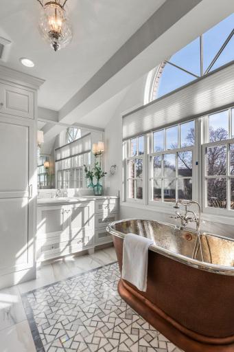 The en-suite bathroom provides a spa-like experience with elegant marble flooring beneath the stunning copper tub.