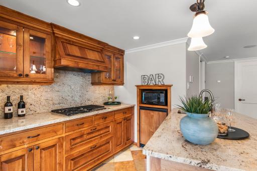 Featuring tile flooring and backsplash, bar seating, timeless wood cabinetry, and premium Wolf appliances with a Scotsman dishwasher and Thermodor warming drawer.