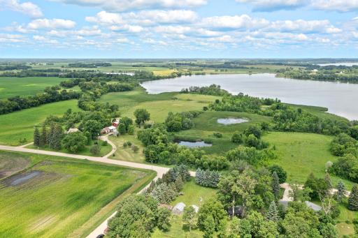 View from across the street looking back at the property. Land extends all the way to treeline on the left, That area is farmland, all the way to the lake in back, includes both wetlands and trees to the right.