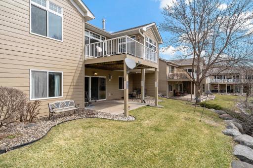 From the back of the property, a closer look at the patio and deck overlooking a retaining wall and wooded area.
