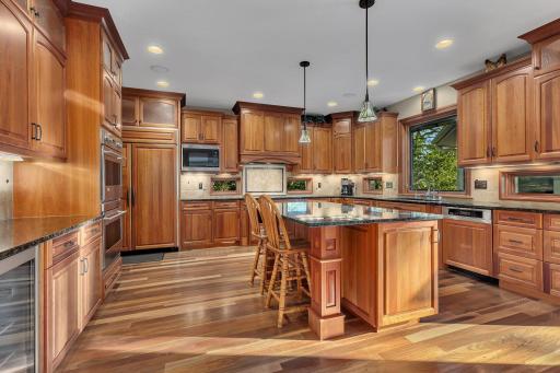 The gourmet kitchen is a culinary masterpiece, featuring granite countertops, a spacious island, double ovens, a beverage fridge, and custom cherry paneled appliances.