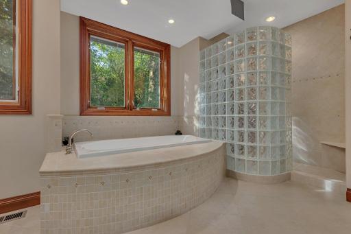 The luxurious soaking tub creates a peaceful space for relaxation. The custom tile surround adds an elegant touch to the curved design. Adjacent is a spacious walk-in shower, featuring a striking glass block wall providing natural light and privacy.