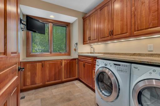This spacious main floor laundry room is both functional and stylish, featuring abundant custom cabinetry for storage, granite countertops, and a convenient utility sink.