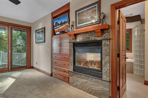 Custom-built cabinetry enhances the rooms functionality and charm, integrating storage and style. A dual-sided fireplace connects the bedroom to the ensuite bathroom, adding warmth and ambiance to both spaces.
