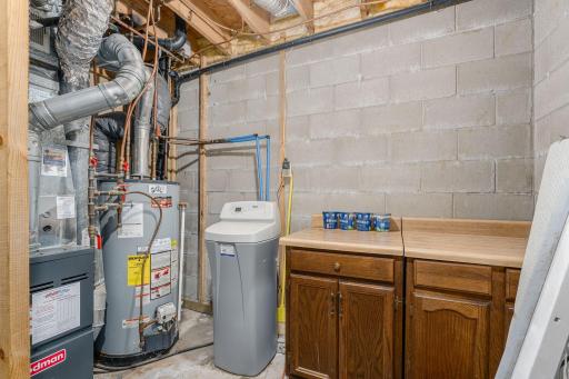 Functional utility room equipped with a water softener, water heater, and additional storage cabinetry.