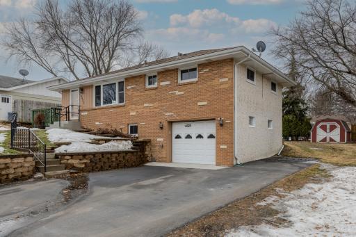 Front Exterior with Garage - Brick veneer front exterior with one-car tuck-under garage and asphalt driveway. Retaining wall and stair access lead to the main entrance. Additional parking space accommodates a boat, trailer, or extra vehicle.