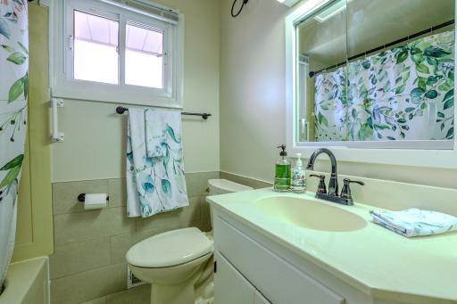 Main-Level Bathroom â Vanity & Tub View â Main-floor bath features a single-sink vanity, updated faucet, mirrored medicine cabinet, and tiled tub surround. A window adds natural light and ventilation, complementing the functional layout.