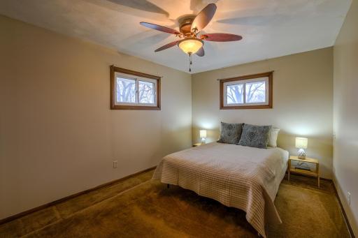 Primary BedroomâBed & Window View â Main-level primary bedroom features dual windows for natural light, neutral walls, and ceiling fan with light. Spacious layout accommodates full bedroom furnishings while maintaining comfortable circulation space.