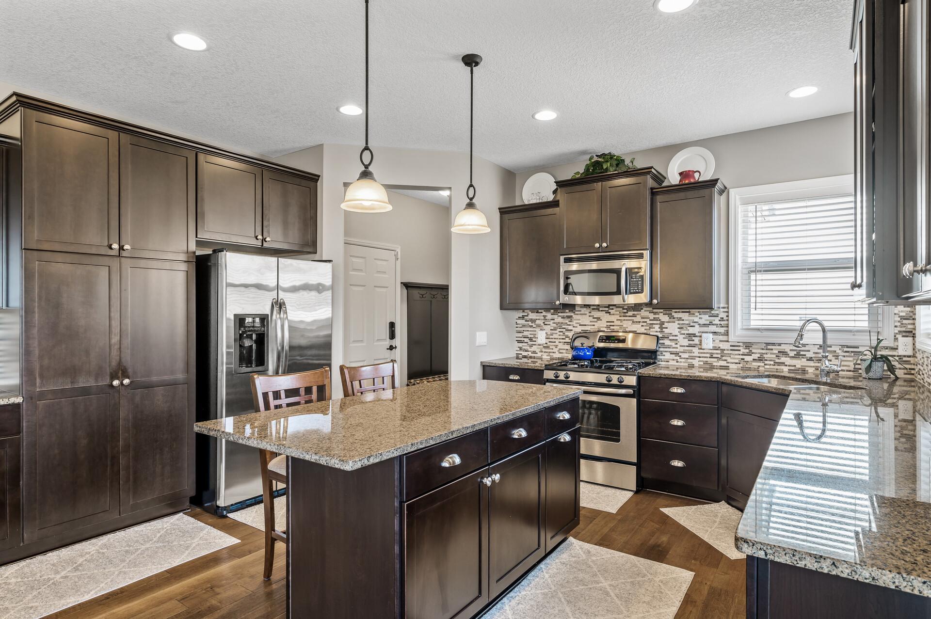 The stunning kitchen features rich wooden cabinetry, sleek countertops, pretty backsplash and stainless steel appliances.
