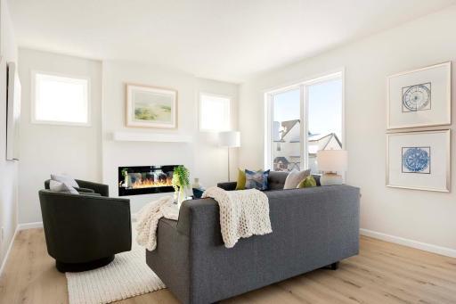 The cozy gathering room is designed to offer warmth and comfort, with well-positioned windows flanking the fireplace, allowing natural light to flood the space. Photos are from previously built home; options and features will vary.