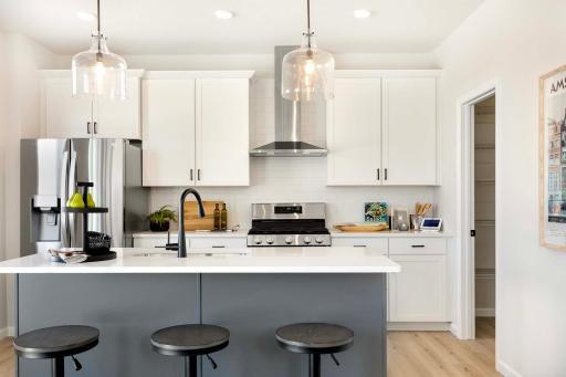 The kitchen island is complemented by designer pendant lighting, adding a touch of sophistication and style. Photos are from previously built home; options and features will vary.