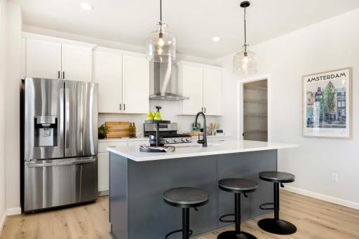 The kitchen features a striking contrast between a sleek gray island and crisp white perimeter cabinets, creating a modern and sophisticated look. Photos are from previously built home; options and features will vary.