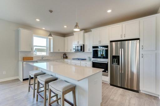 A stunning kitchen with ample counter space, including a 7-foot island provides the perfect setting for entertaining guests. Your white kitchen will have black pendants and hardware. Photo of model home, other finishes will vary.