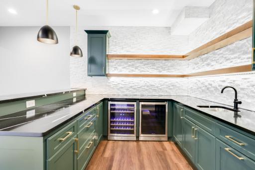 The large wet bar features separate wine and beverage fridges, open shelving and quartz tops.