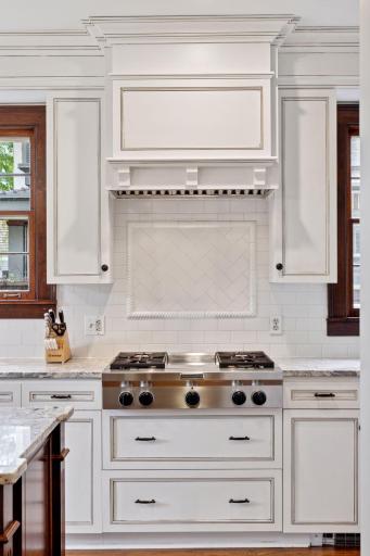 A four burner gas cooktop with neutral subway tile backsplash and wooden stove hood.