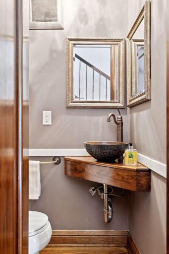 Main level powder room with unique corner vanity made of dark wood, supporting a decorative sink bowl and bronze-toned faucet.