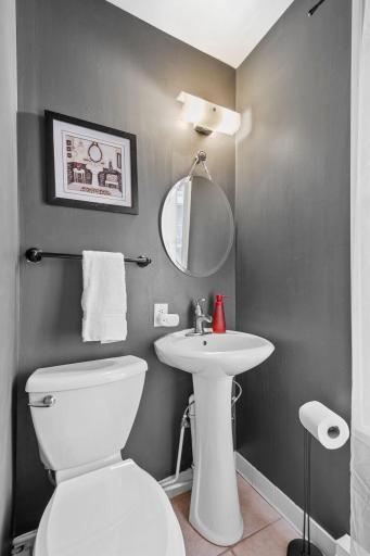 This sleek and modern half bath features a pedestal sink, round mirror, and contemporary lighting against a bold, dark-painted wallâperfectly blending function and style.
